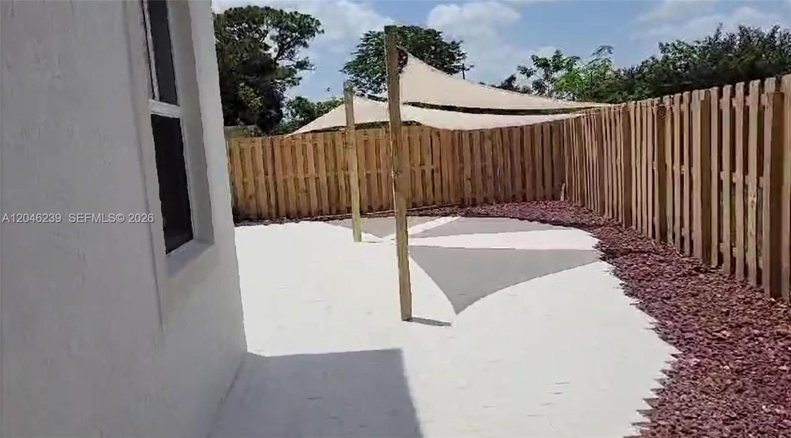 A backyard patio features a white concrete surface, a wooden fence, and shade sails — 2439 NW 131st Cir, Miami FL 33167, MIAMI, FL