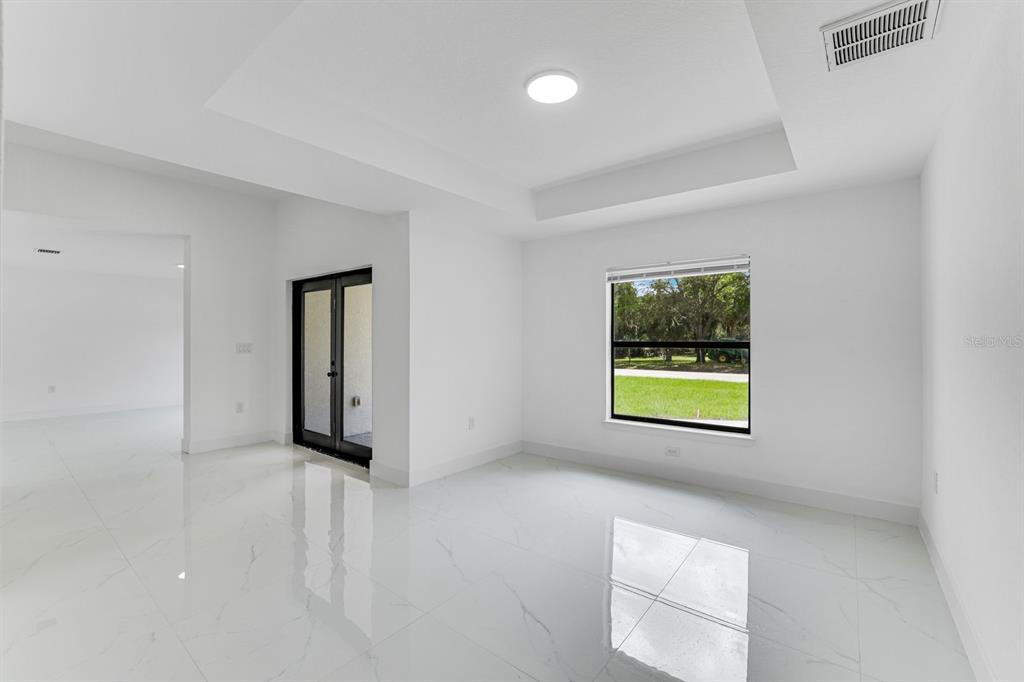 A bright, empty room with white tile floors, a tray ceiling, and a glass door — 2702 50TH STREET SW, LEHIGH ACRES, FL