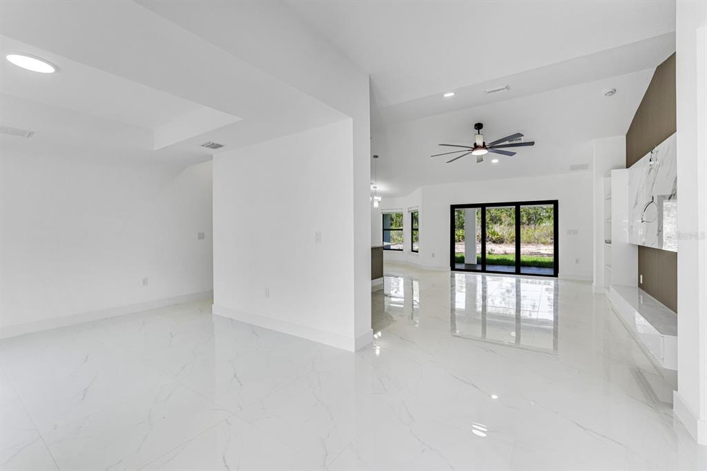 A bright, open-concept living area features white marble-look tile flooring and a large sliding glass door — 2702 50TH STREET SW, LEHIGH ACRES, FL