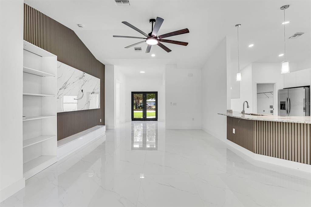 A bright, open-concept living area features white tile floors, a slatted wood wall, and kitchen — 2702 50TH STREET SW, LEHIGH ACRES, FL