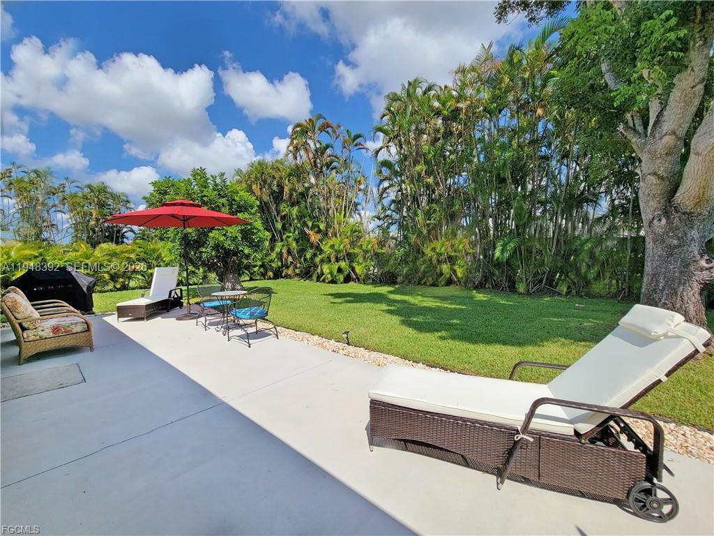 A backyard patio features lounge chairs, a red umbrella, and a grassy lawn with trees — 237 SW 47TH ST # 0, Cape Coral FL 33914, CAPE CORAL, FL