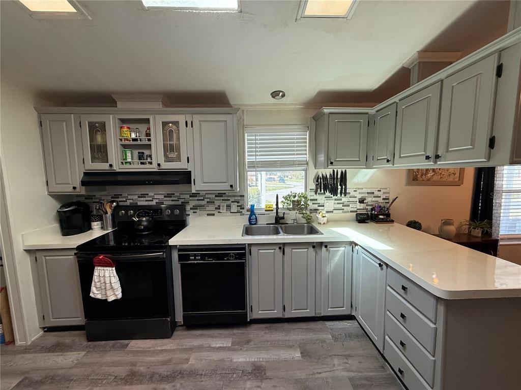 A kitchen features grey cabinets, white countertops, a black stove, and a tile backsplash — 5255 OXFORD COURT, WILDWOOD, FL