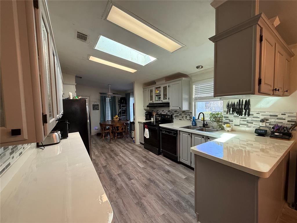 A kitchen with light gray cabinets, white countertops, stainless appliances, and wood-look flooring — 5255 OXFORD COURT, WILDWOOD, FL