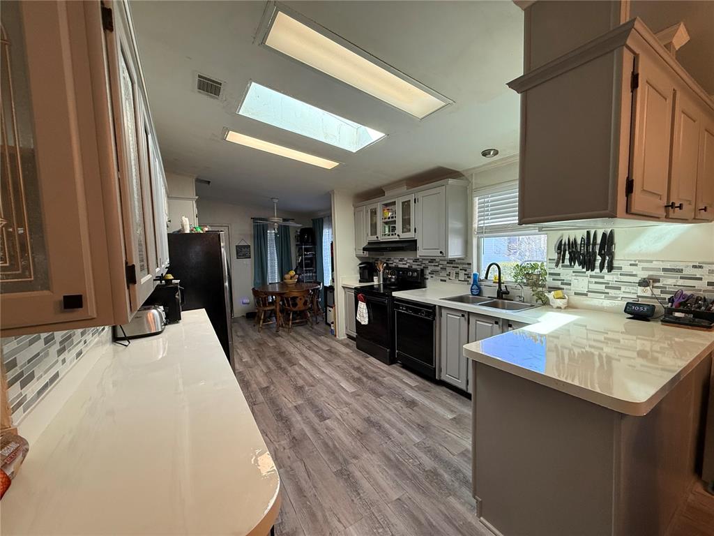 A kitchen features gray cabinets, white countertops, a tile backsplash, and wood-look flooring — 5255 OXFORD COURT, WILDWOOD, FL