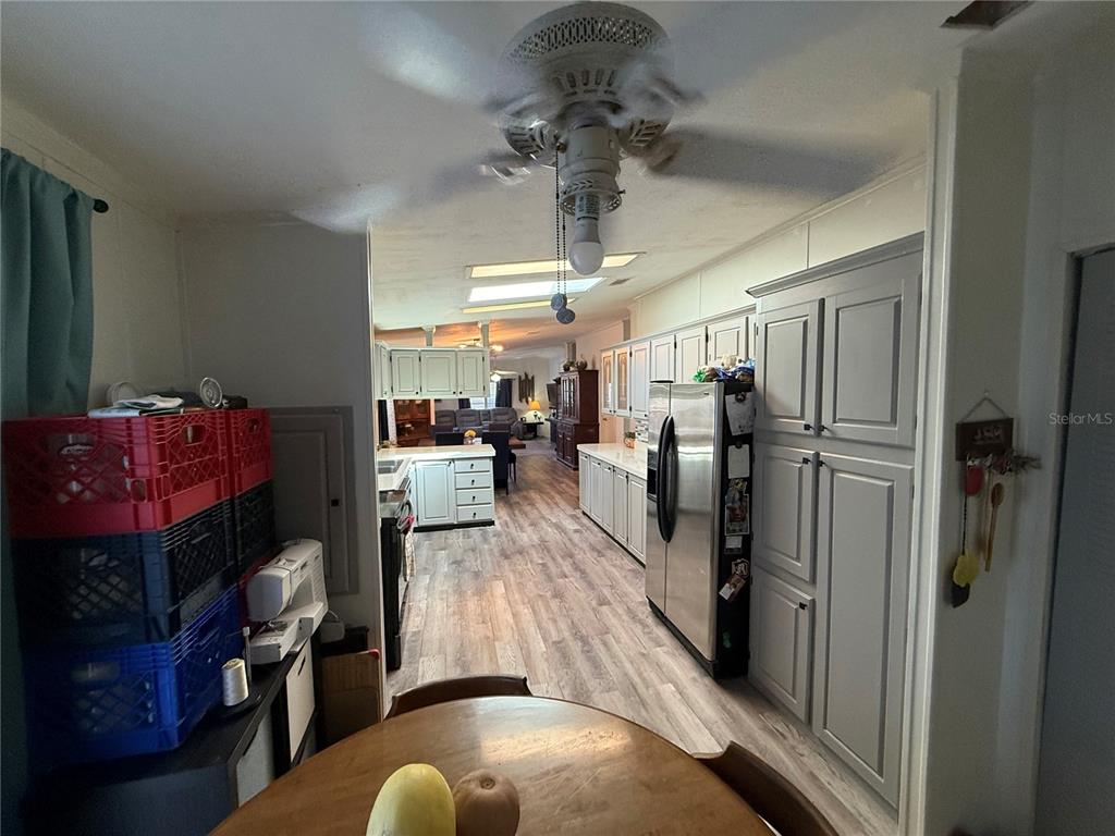 A kitchen with light-colored cabinets, stainless steel appliances, and wood-look flooring leads to a living area — 5255 OXFORD COURT, WILDWOOD, FL