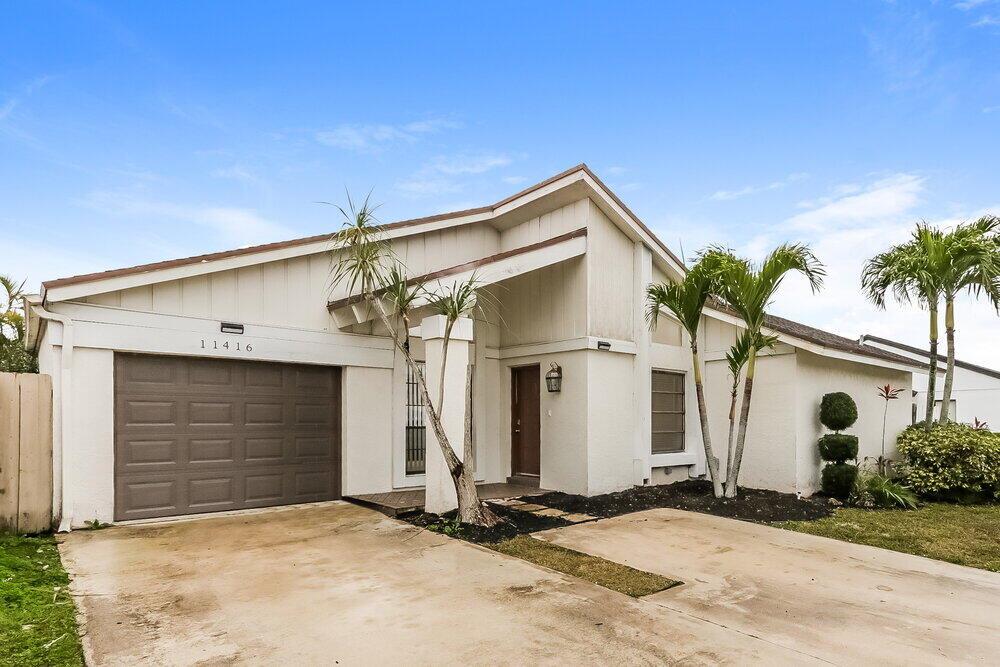 A single-story house with a brown garage door, white exterior, and palm trees in front — BOCA RATON, FL