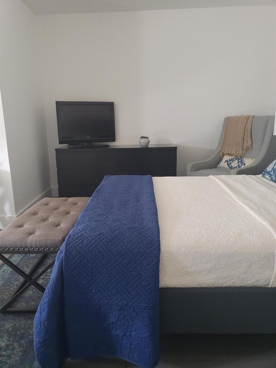 A bedroom features a bed with a blue quilt, a dresser with a television, and seating — 14313 N Flora Lane # A, Wellington FL 33414, WELLINGTON, FL
