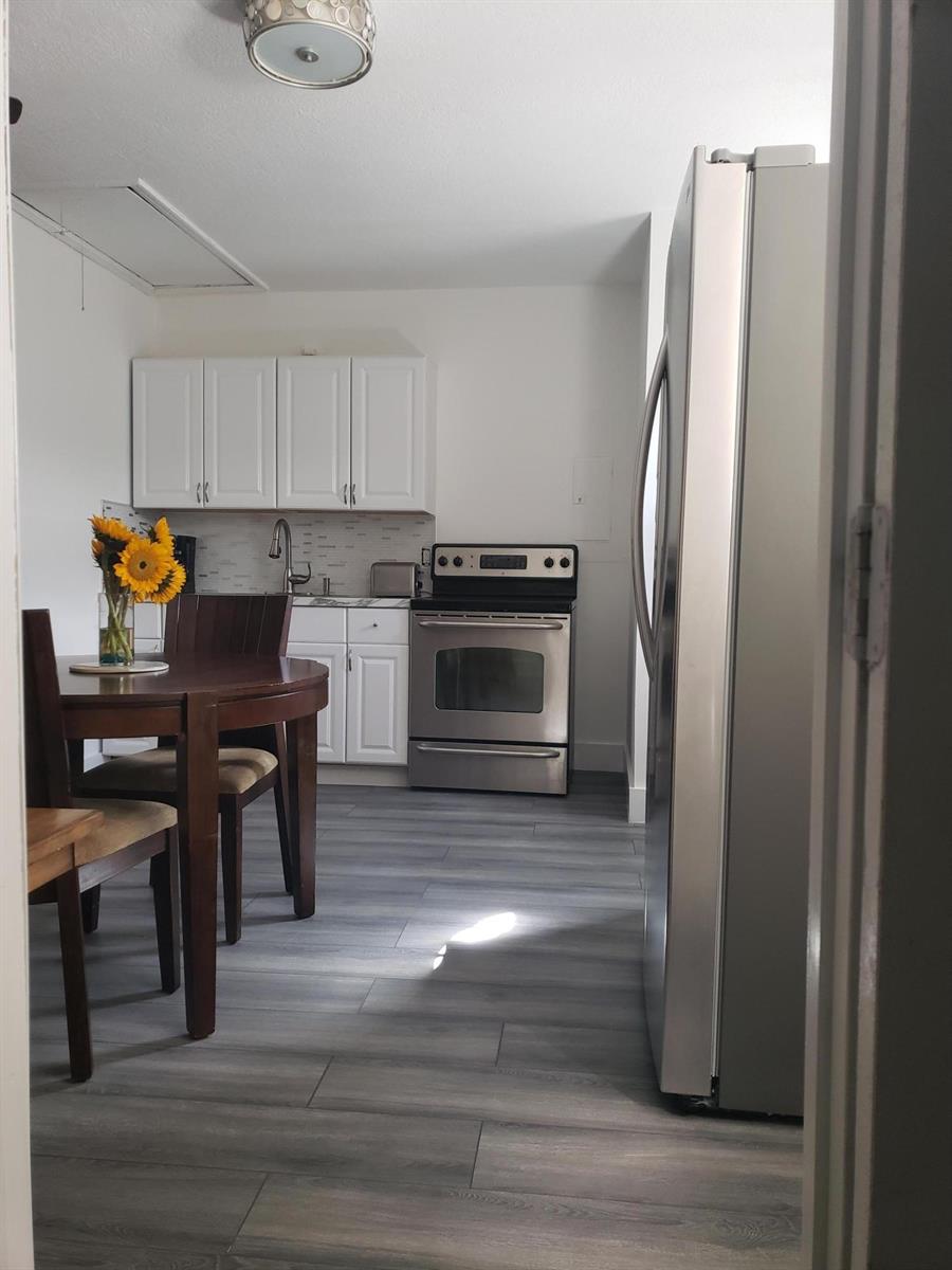 A kitchen features white cabinets, stainless steel appliances, and wood-look flooring with a dining set — 14313 N Flora Lane # A, Wellington FL 33414, WELLINGTON, FL