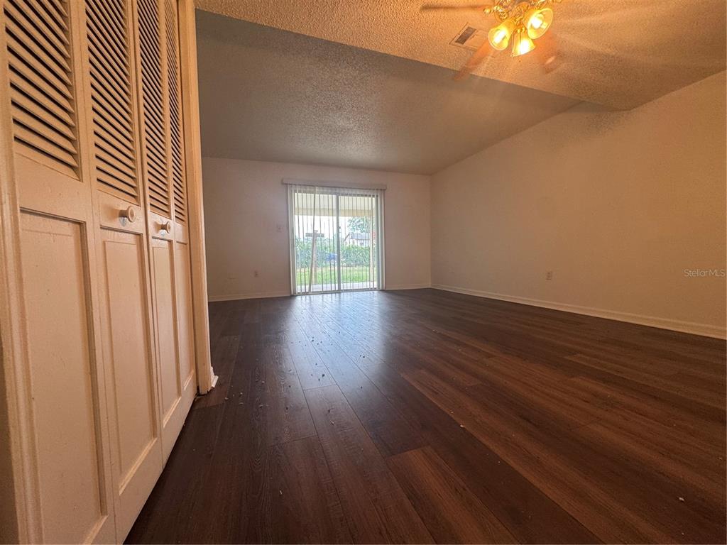An empty room features dark wood-look flooring, white walls, and a sliding glass door — 221 S CYPRESS WAY, CASSELBERRY, FL