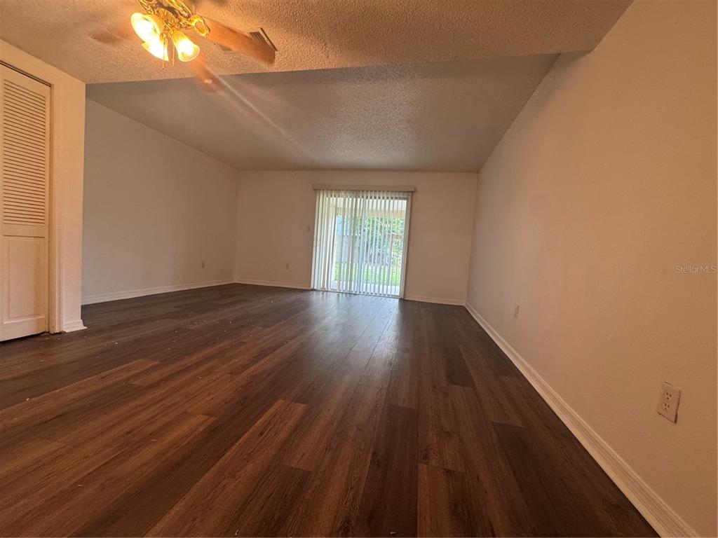 An empty living room features dark wood-look flooring, white walls, and a sliding glass door — 221 S CYPRESS WAY, CASSELBERRY, FL