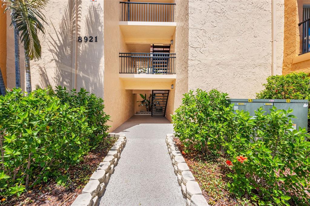 An exterior view of a multi-story apartment building with a concrete walkway and metal stairs — 8921 BLIND PASS ROAD UNIT 141, ST PETE BEACH, FL