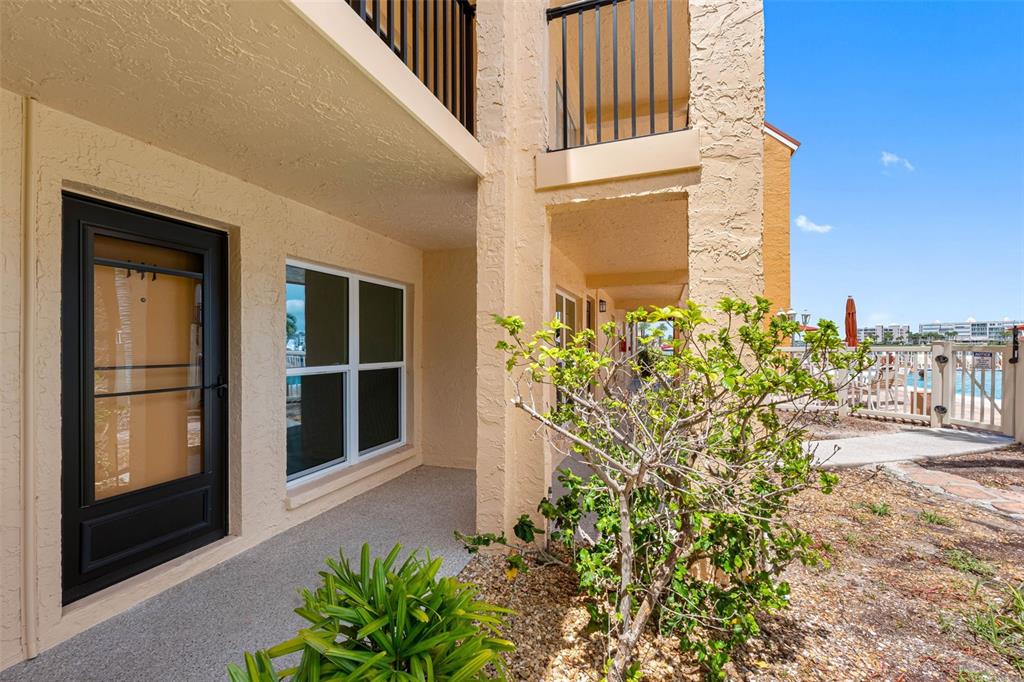 A ground-level apartment entrance with a black storm door, window, and adjacent landscaping — 8921 BLIND PASS ROAD UNIT 141, ST PETE BEACH, FL