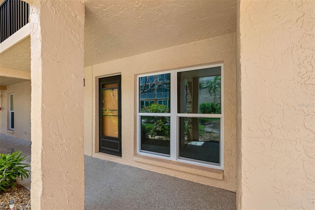 A covered patio features a dark front door and a large window on a stucco wall — 8921 BLIND PASS ROAD UNIT 141, ST PETE BEACH, FL