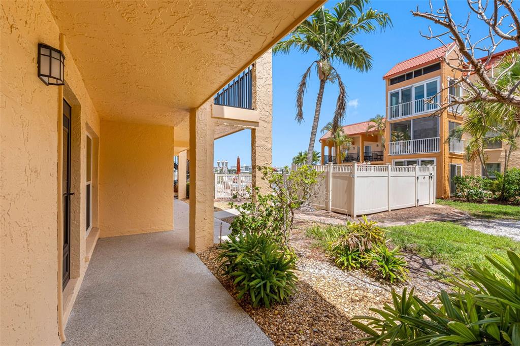 A covered patio with a concrete floor overlooks a landscaped yard and a nearby building — 8921 BLIND PASS ROAD UNIT 141, ST PETE BEACH, FL