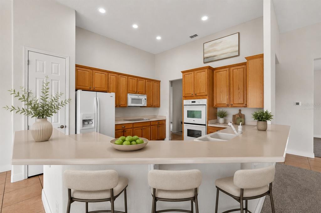 A kitchen features wood cabinets, light countertops, a breakfast bar with stools, and recessed lighting — 453 SORRENTO RD, KISSIMMEE, FL