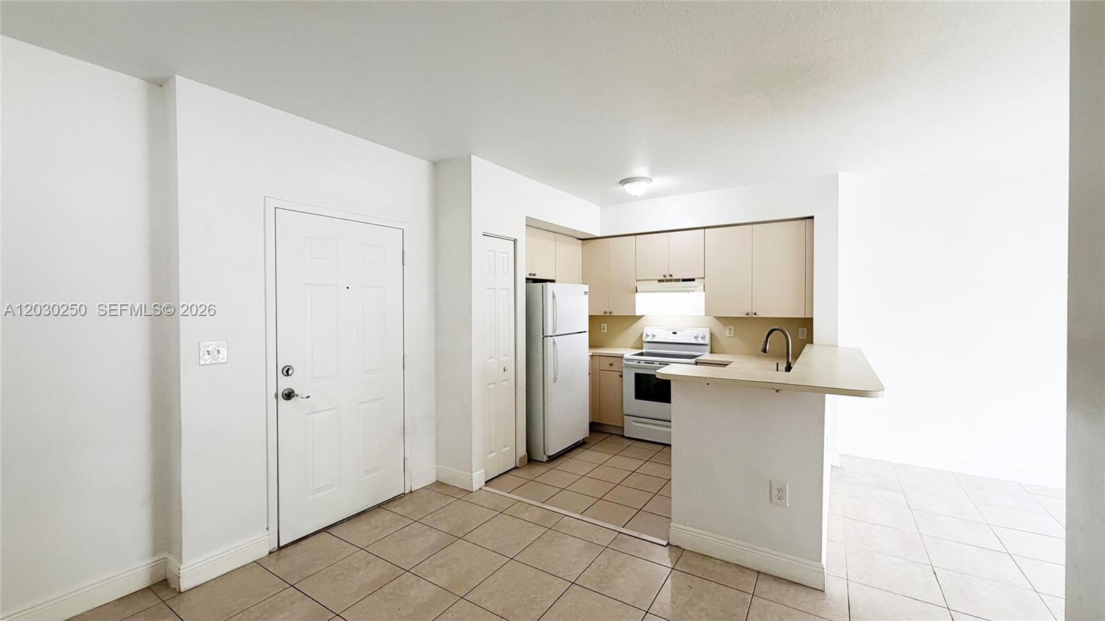 This kitchen features light-colored cabinets, white appliances, and tiled flooring with an attached breakfast bar — CUTLER BAY, FL