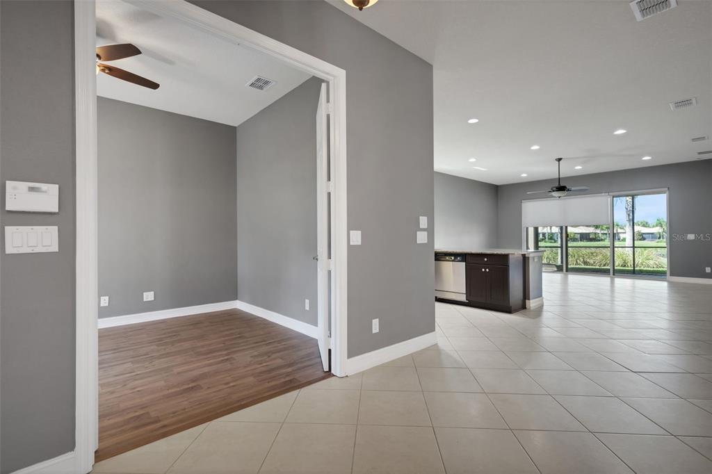 A room with wood flooring and gray walls opens into a tiled kitchen and living area — 15841 COBBLE MILL DRIVE, WIMAUMA, FL