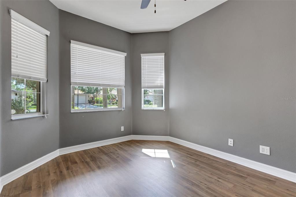 An empty room with gray walls, wood-look flooring, and three windows with white blinds — 15841 COBBLE MILL DRIVE, WIMAUMA, FL