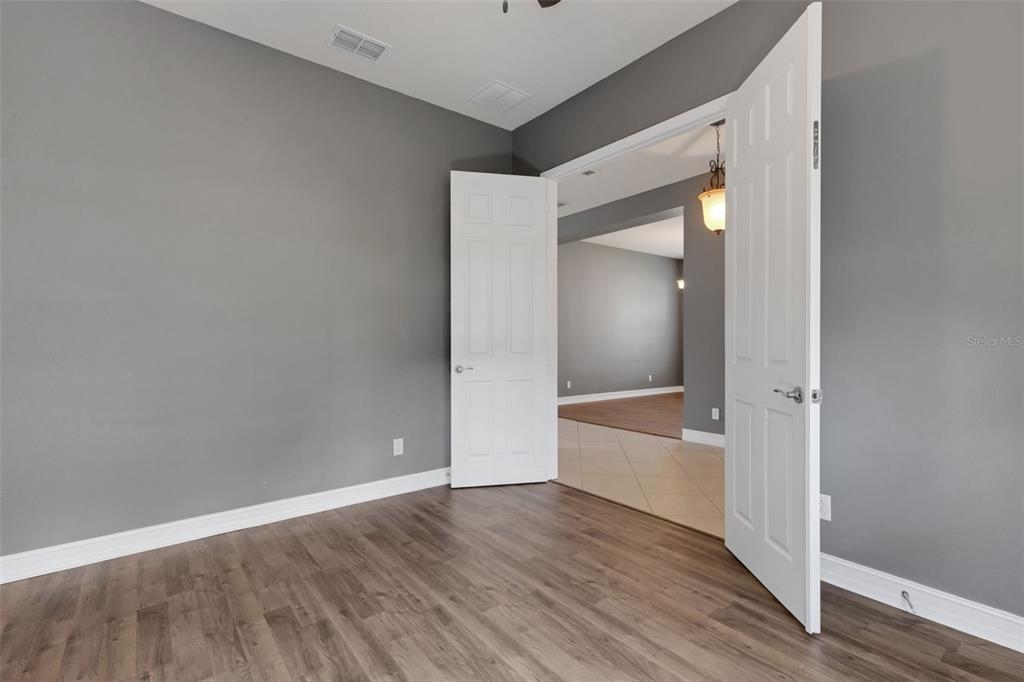 A room with gray walls and wood-look flooring leads through double doors into another space — 15841 COBBLE MILL DRIVE, WIMAUMA, FL