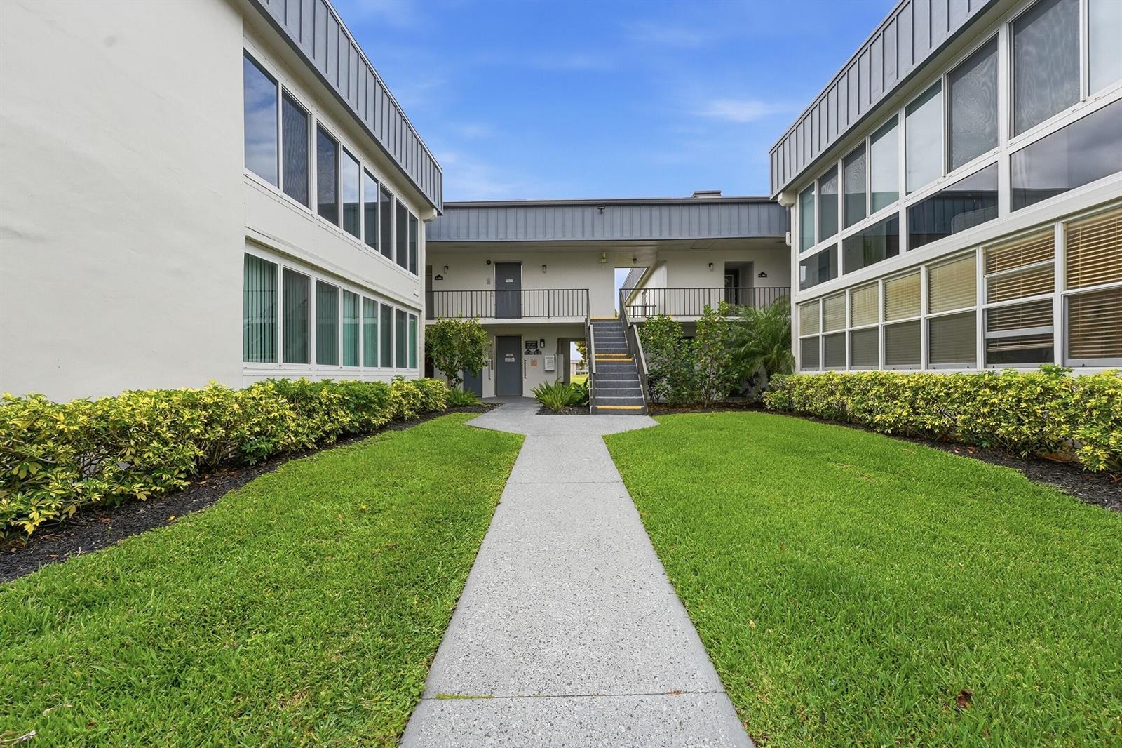 A concrete walkway leads to a two-story apartment building with stairs and green landscaping — 566 Piedmont L, Delray Beach FL 33484, DELRAY BEACH, FL