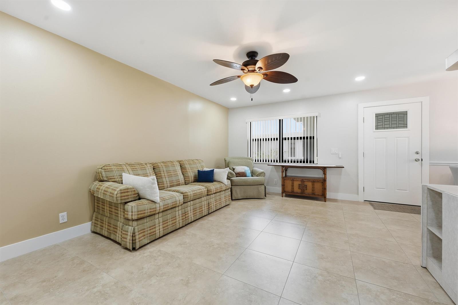 A living room features beige walls, tile flooring, a plaid sofa, and a ceiling fan — 566 Piedmont L, Delray Beach FL 33484, DELRAY BEACH, FL