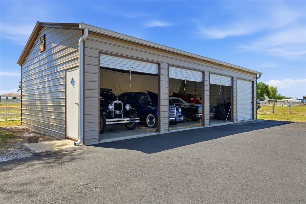 A metal garage with three open bays containing vintage cars sits on a paved lot — 15470 STATE ROAD 62, PARRISH, FL