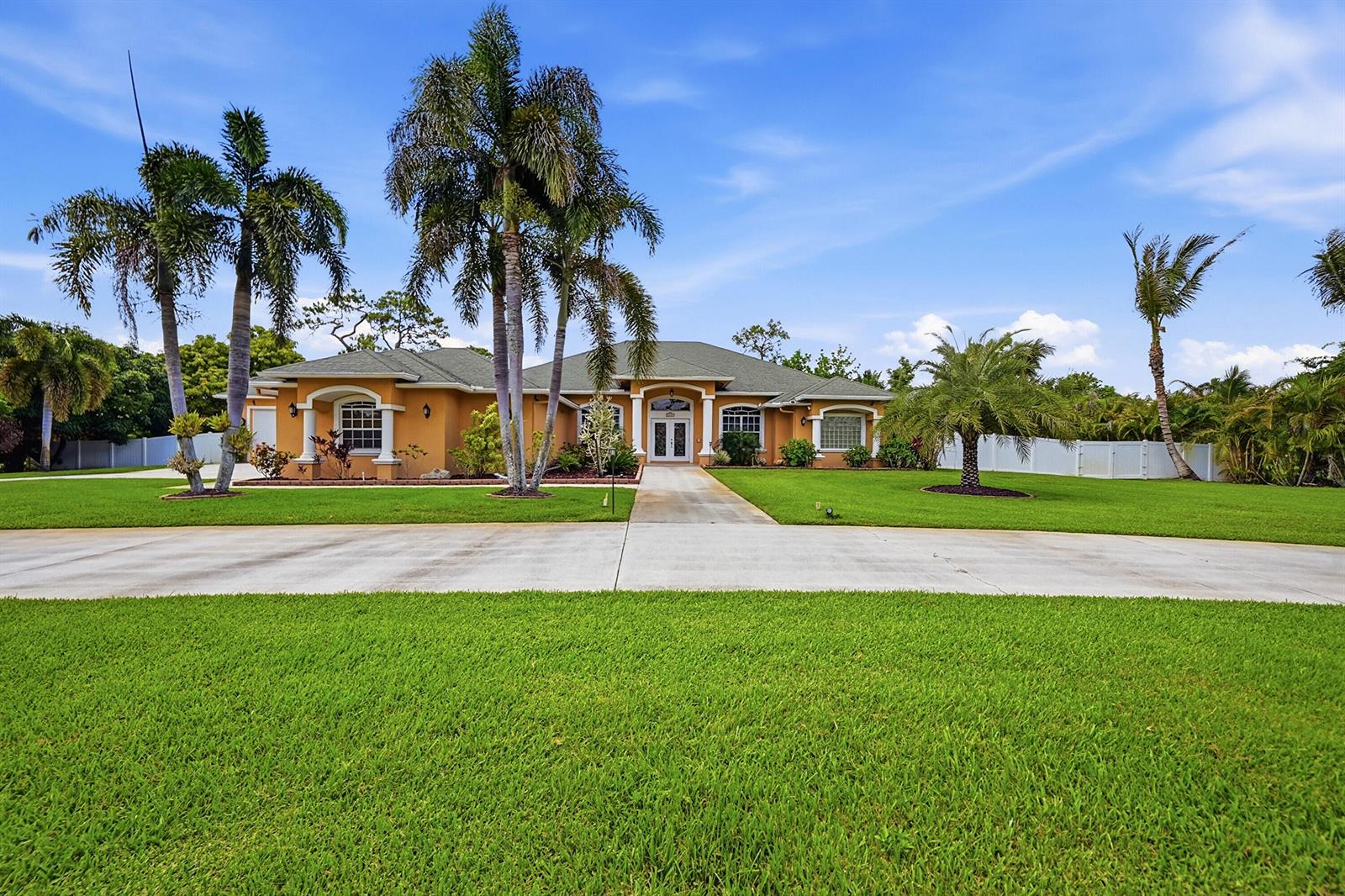 A single-story, tan-colored house with a concrete driveway and palm trees on a grassy lawn — 14310 N 85th Rd Road N, FL 33470, FL