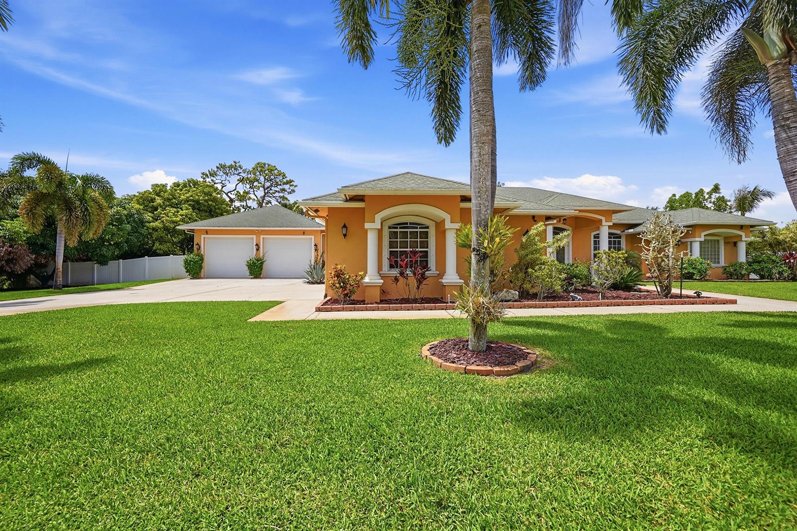 A single-story orange house with a two-car garage and palm trees on a sunny day — 14310 N 85th Rd Road N, FL 33470, FL
