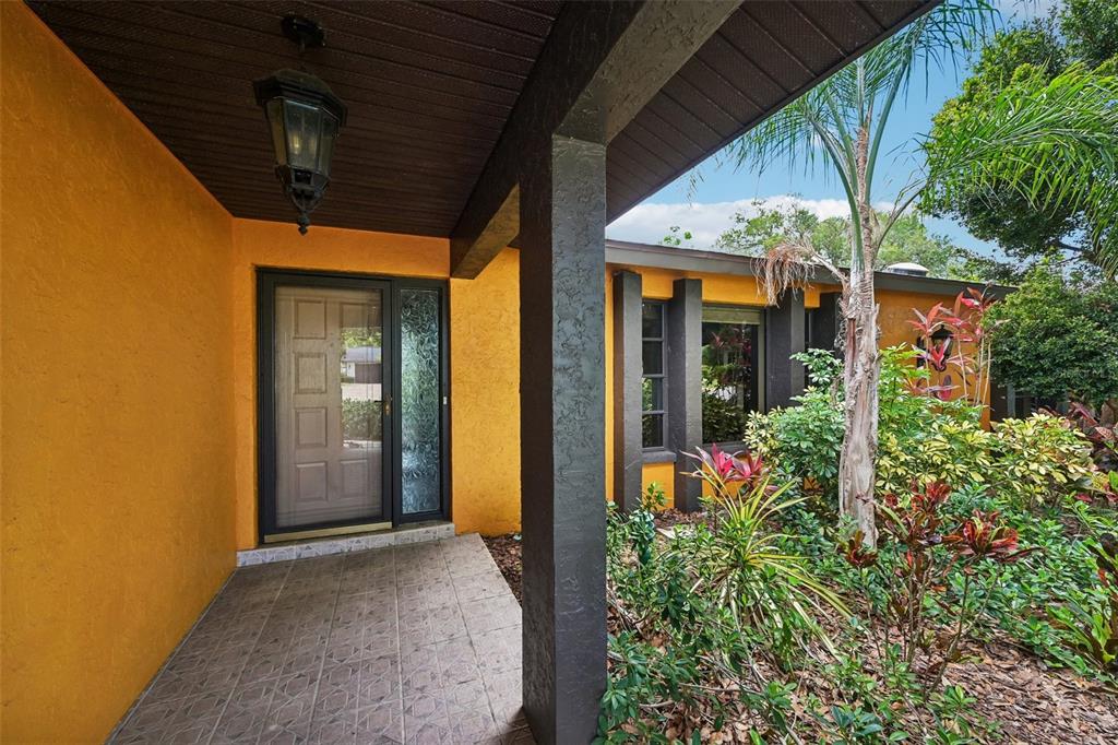 The exterior of a house features a yellow stucco wall, a covered porch, and landscaping — 4873 HUNTLEIGH DRIVE, SARASOTA, FL