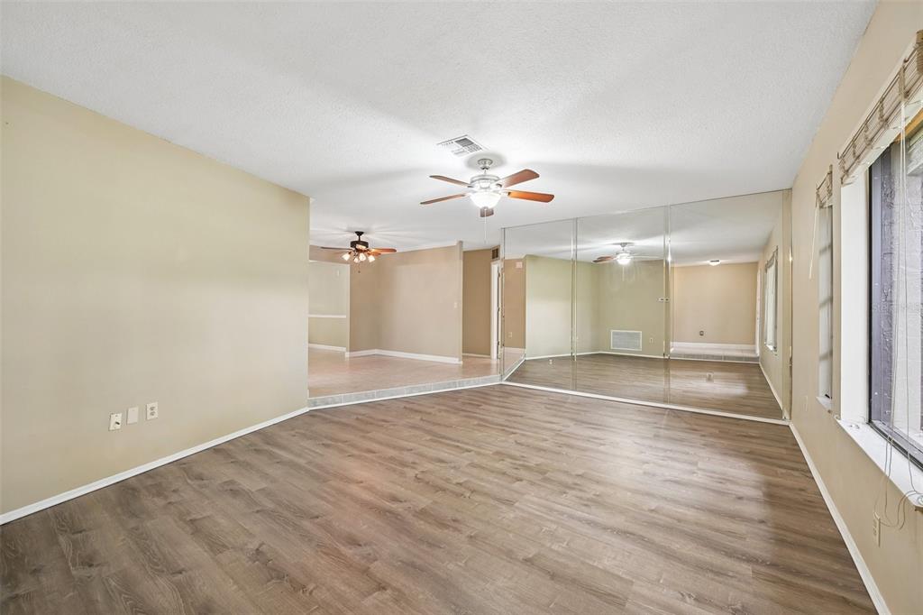 A living room with wood-look flooring, a ceiling fan, and a wall of mirrored closet doors — 4873 HUNTLEIGH DRIVE, SARASOTA, FL