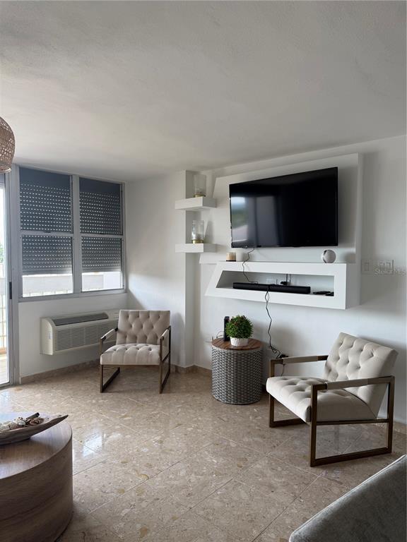 A living room features two tufted armchairs, a wall-mounted television, and light-colored tile flooring — 3001 ave isla verde PLAZA DEL MAR UNIT 405, CAROLINA, PR