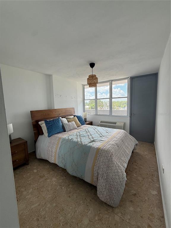 A bedroom features a wooden bed frame, tile flooring, a hanging light fixture, and windows — 3001 ave isla verde PLAZA DEL MAR UNIT 405, CAROLINA, PR