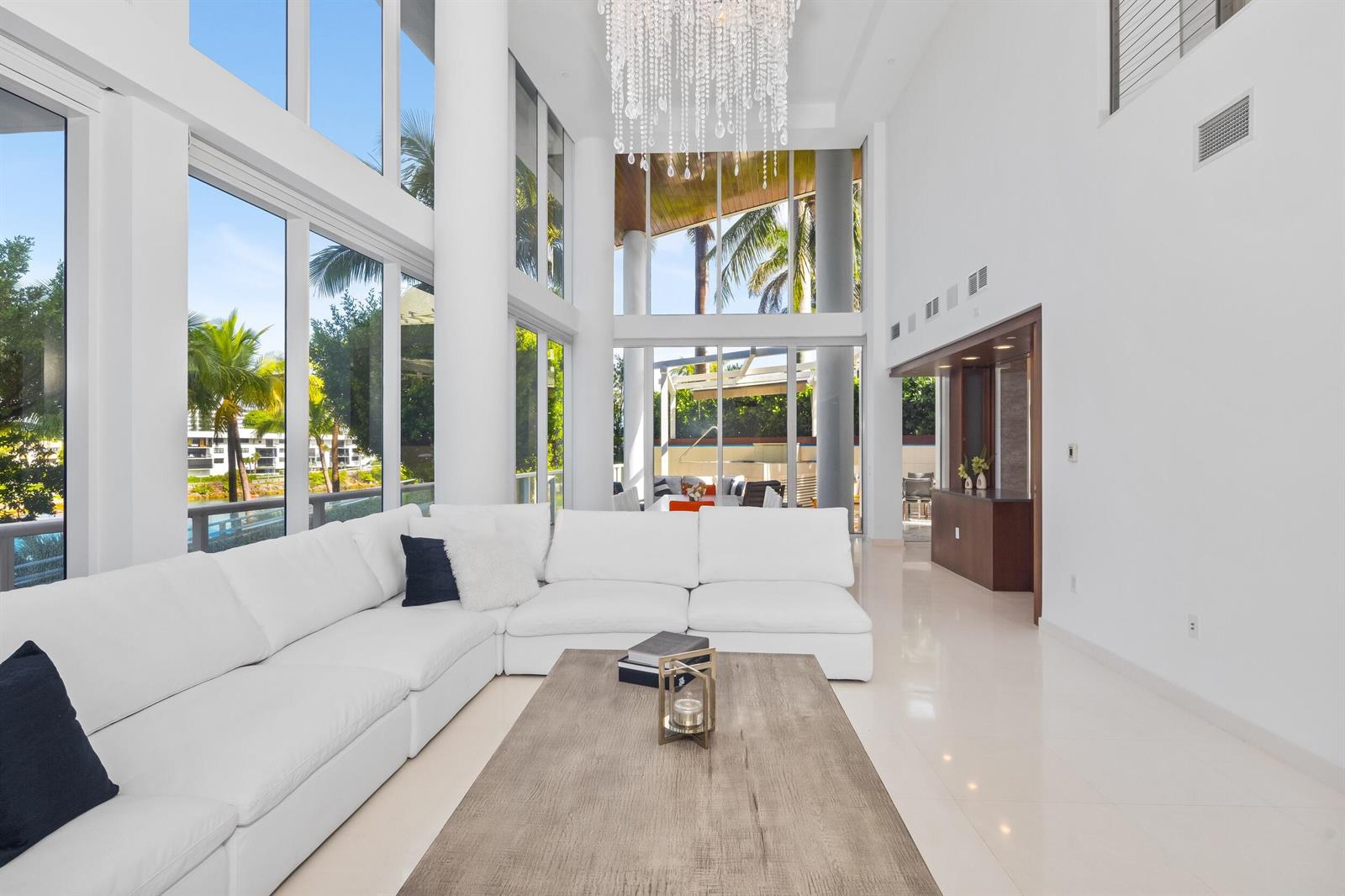 A bright, double-height living room features a large white sectional, wood coffee table, and chandelier — 1000 S Ocean Boulevard # 110, Boca Raton FL 33432, BOCA RATON, FL
