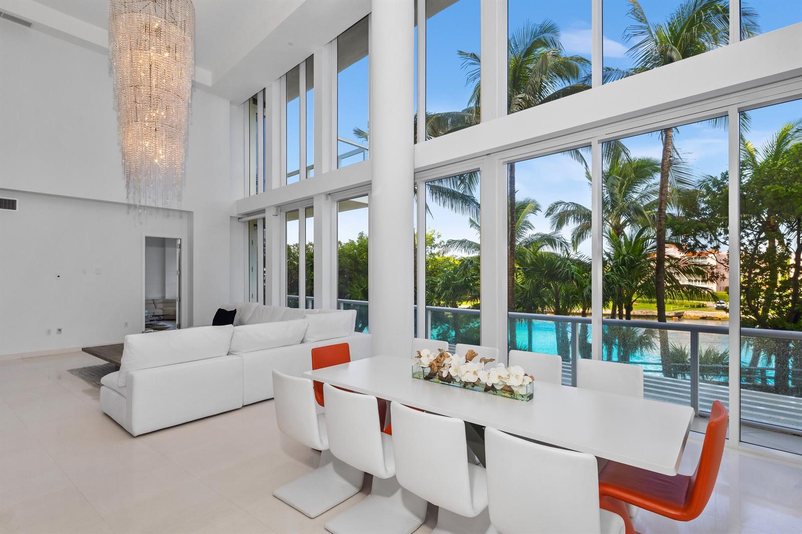 A modern dining and living area features a crystal chandelier, white furniture, and floor-to-ceiling windows — 1000 S Ocean Boulevard # 110, Boca Raton FL 33432, BOCA RATON, FL
