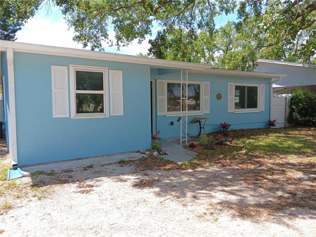 A light blue single-story house features white shutters, a gravel driveway, and mature trees — 7980 52ND STREET N, PINELLAS PARK, FL