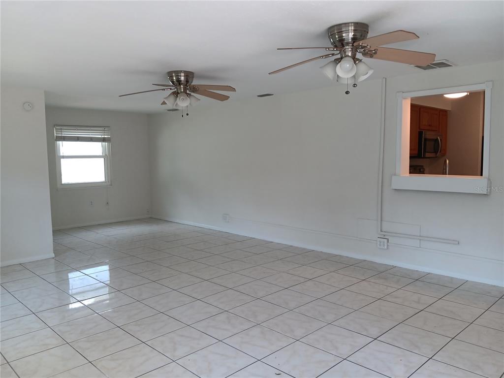 An empty room with white tile floors, two ceiling fans, and a kitchen pass-through window — 7980 52ND STREET N, PINELLAS PARK, FL