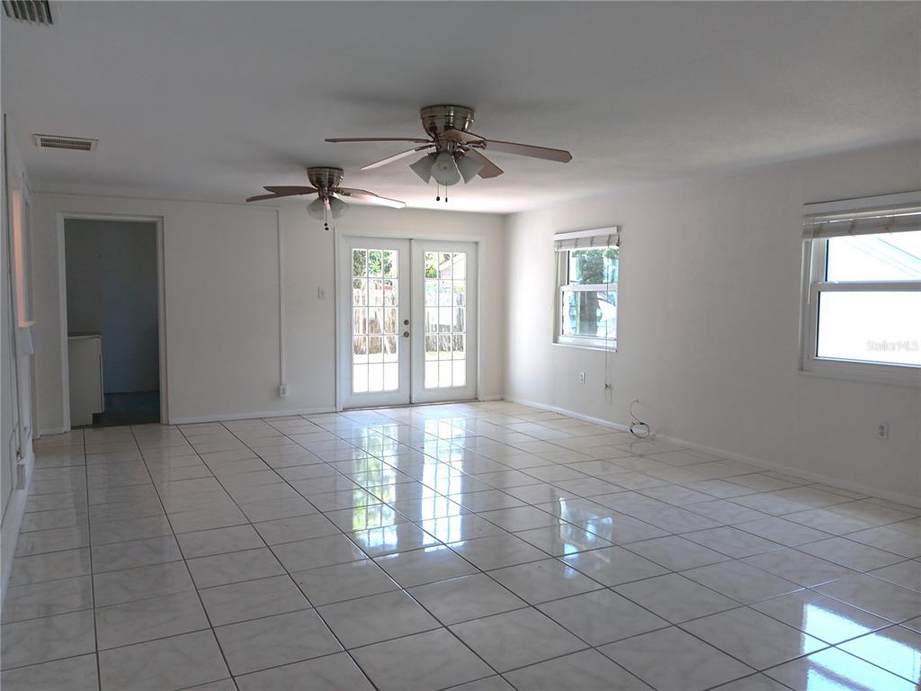 A bright, empty room features white walls, tiled flooring, two ceiling fans, and glass doors — 7980 52ND STREET N, PINELLAS PARK, FL