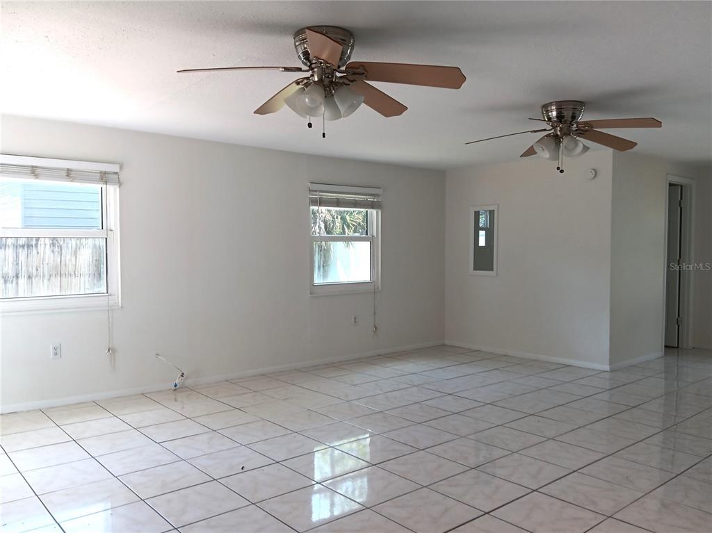 A bright, empty room features white tile flooring, two ceiling fans, and two windows — 7980 52ND STREET N, PINELLAS PARK, FL