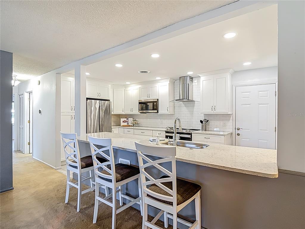 A kitchen features white cabinets, stainless steel appliances, a quartz island, and three bar stools — 11431 DOLLAR LAKE DRIVE UNIT 1, PORT RICHEY, FL