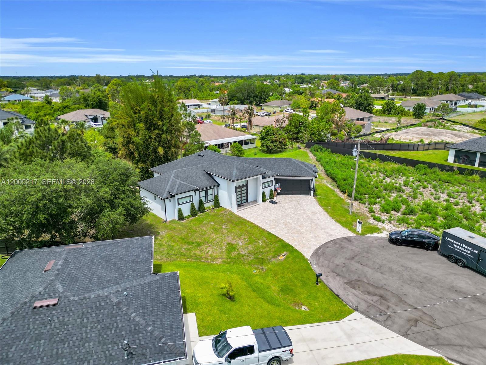 An aerial view shows a modern white house with a dark roof and paved driveway — 3510 W 9th Ct, Lehigh Acres FL 33971, LEHIGH ACRES, FL