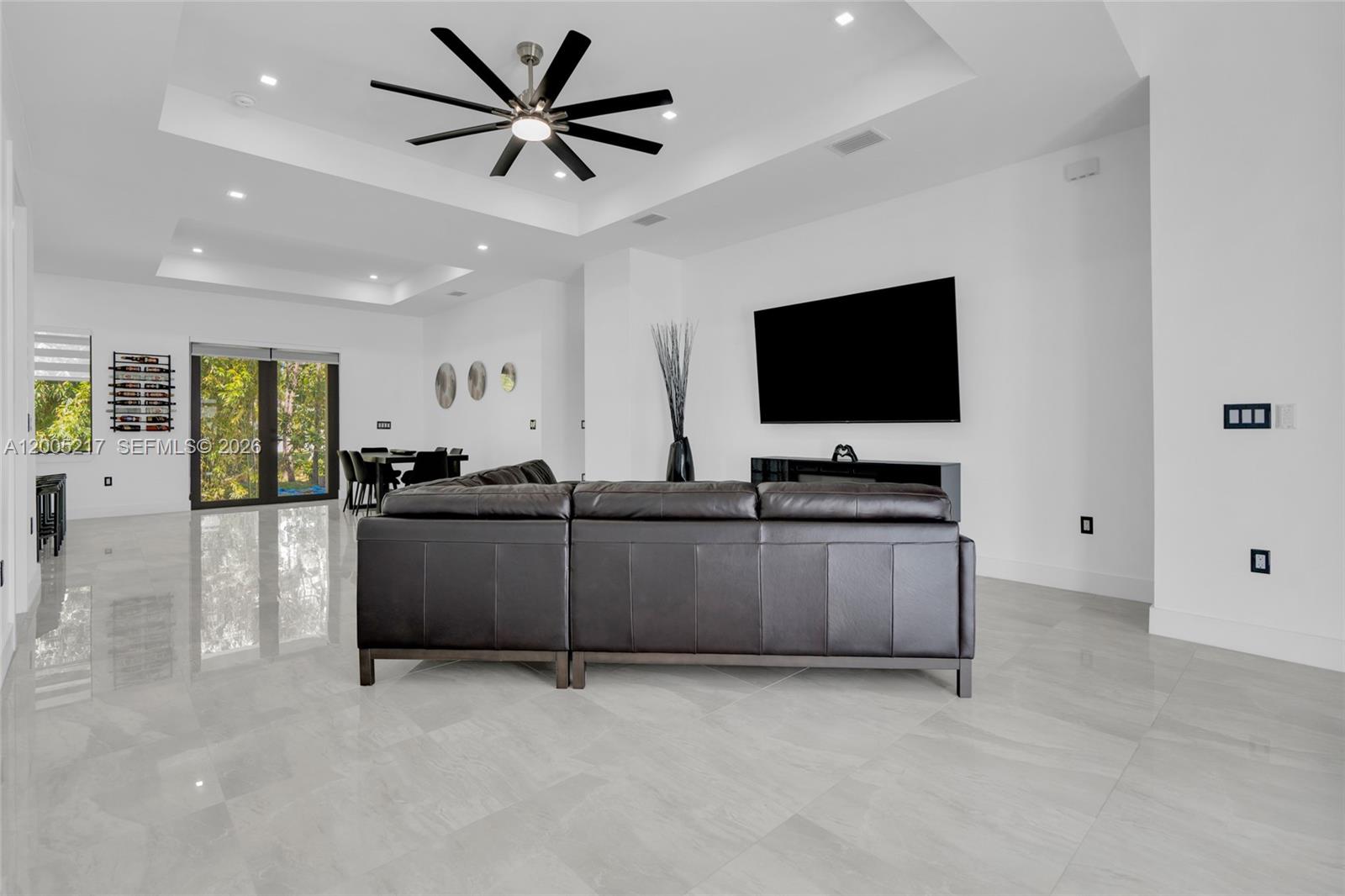 A modern living room features a dark leather sectional, a large television, and tile flooring — 3510 W 9th Ct, Lehigh Acres FL 33971, LEHIGH ACRES, FL