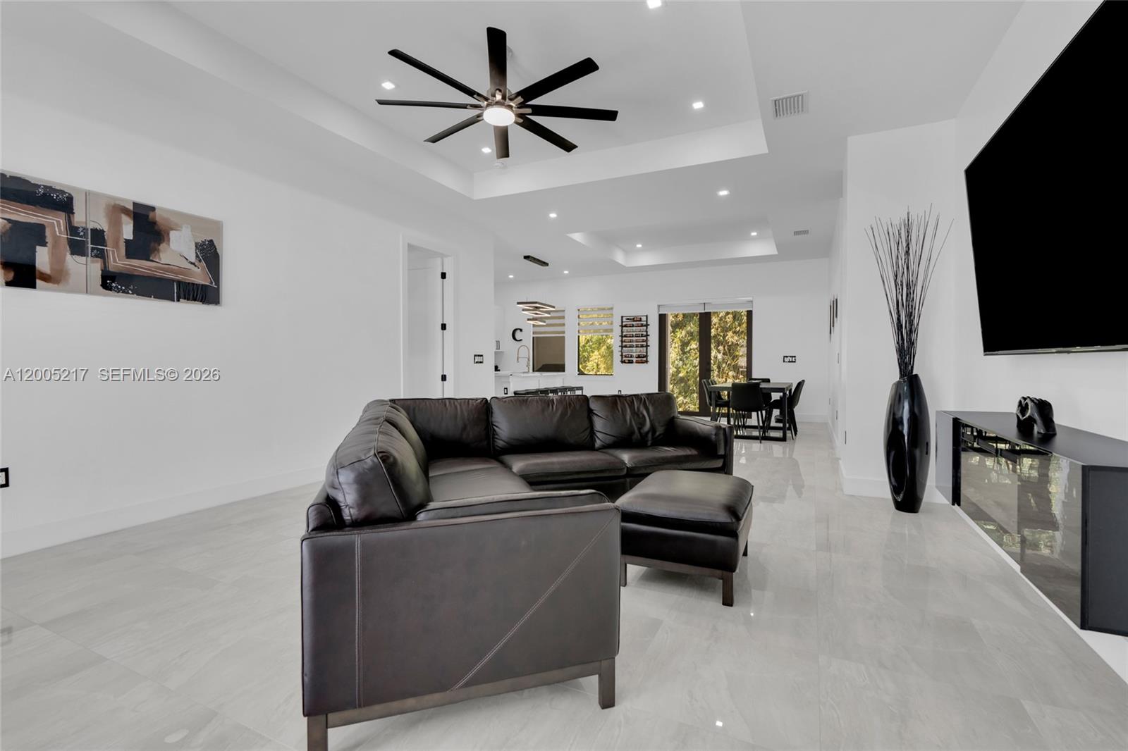 A modern living room features a black sectional sofa, tile flooring, and a tray ceiling — 3510 W 9th Ct, Lehigh Acres FL 33971, LEHIGH ACRES, FL
