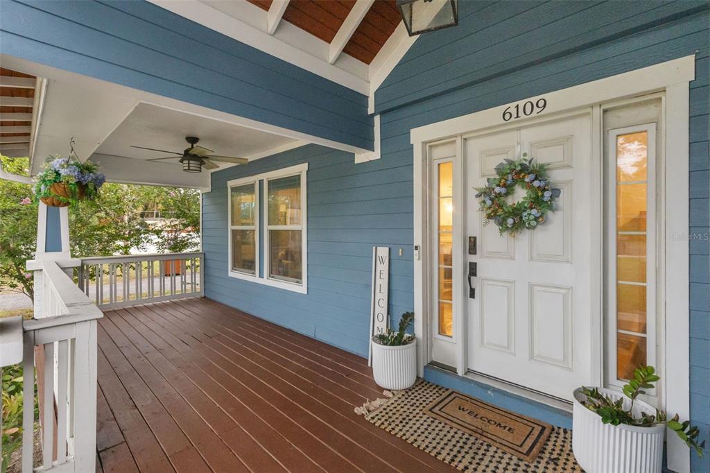 A blue-sided house features a covered wooden porch with a white front door and wreath — 6109 N 22ND STREET, TAMPA, FL
