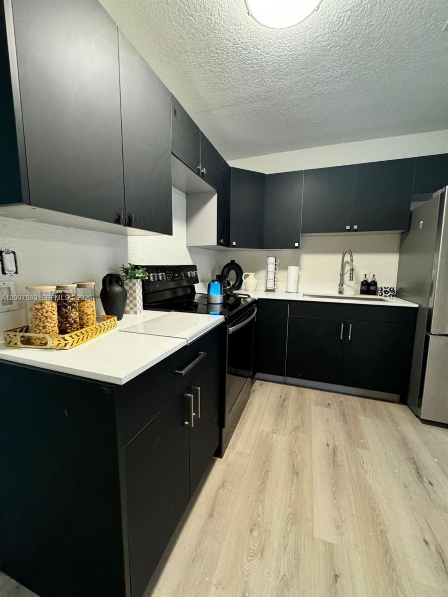 A kitchen features black cabinets, white countertops, stainless steel appliances, and light wood-look flooring — 1865 NW 45th St # 1, Miami FL 33142, MIAMI, FL