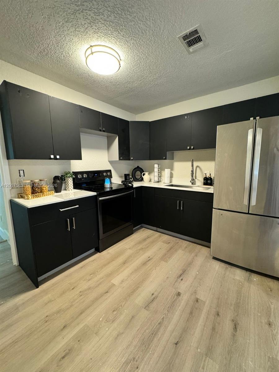 A kitchen features black cabinets, stainless steel appliances, white countertops, and light wood-look flooring — 1865 NW 45th St # 1, Miami FL 33142, MIAMI, FL