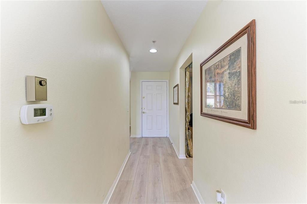 A hallway with light wood-look flooring leads to a white front door — 5350 HYLAND HILLS AVENUE UNIT 2512, SARASOTA, FL