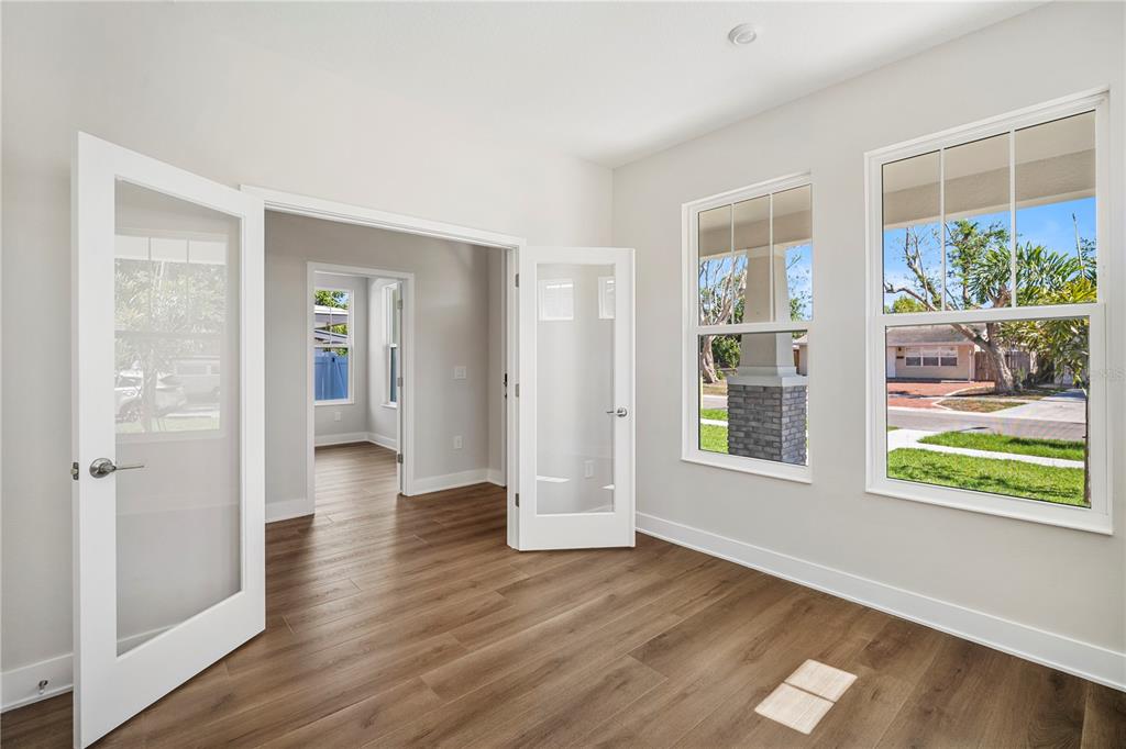 An interior room features light-colored walls, wood-look flooring, French doors, and two large windows — 5633 DARTMOUTH AVENUE N, ST PETERSBURG, FL