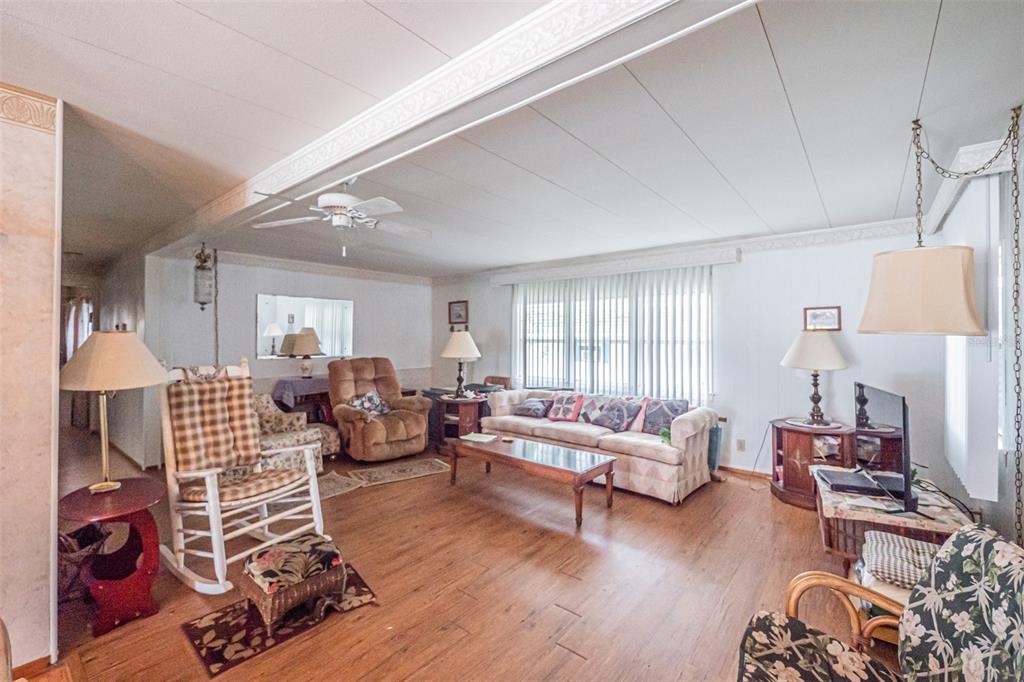 A living room with wood-look flooring, a beige sofa, a rocking chair, and a ceiling fan — 613 SANDPIPER DRIVE, LEESBURG, FL
