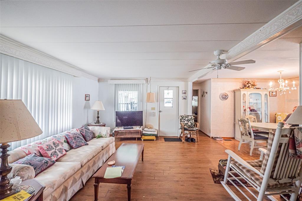 A living room with wood-look flooring, a sofa, a television, and an adjacent dining area — 613 SANDPIPER DRIVE, LEESBURG, FL
