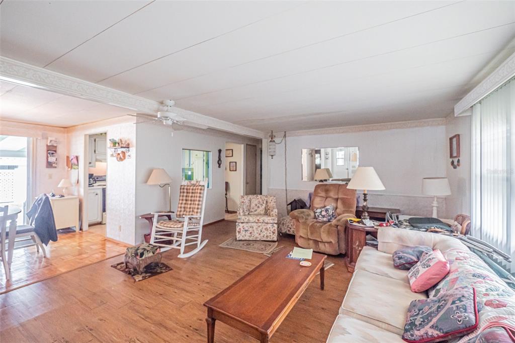 A living room with wood-look flooring, a sofa, armchairs, a coffee table, and a ceiling fan — 613 SANDPIPER DRIVE, LEESBURG, FL